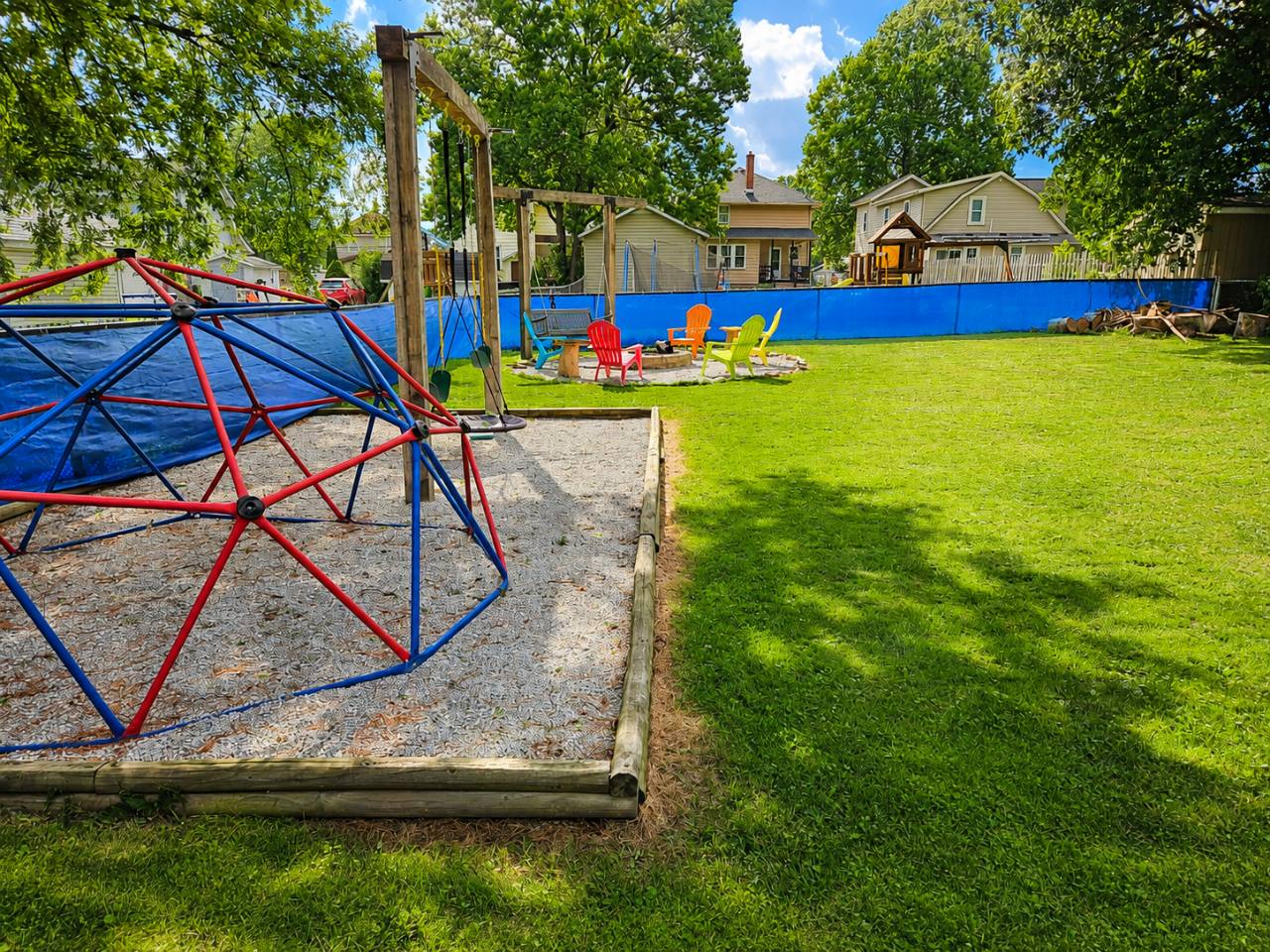 Red and blue climbing dome beside swings and a grassy fenced backyard