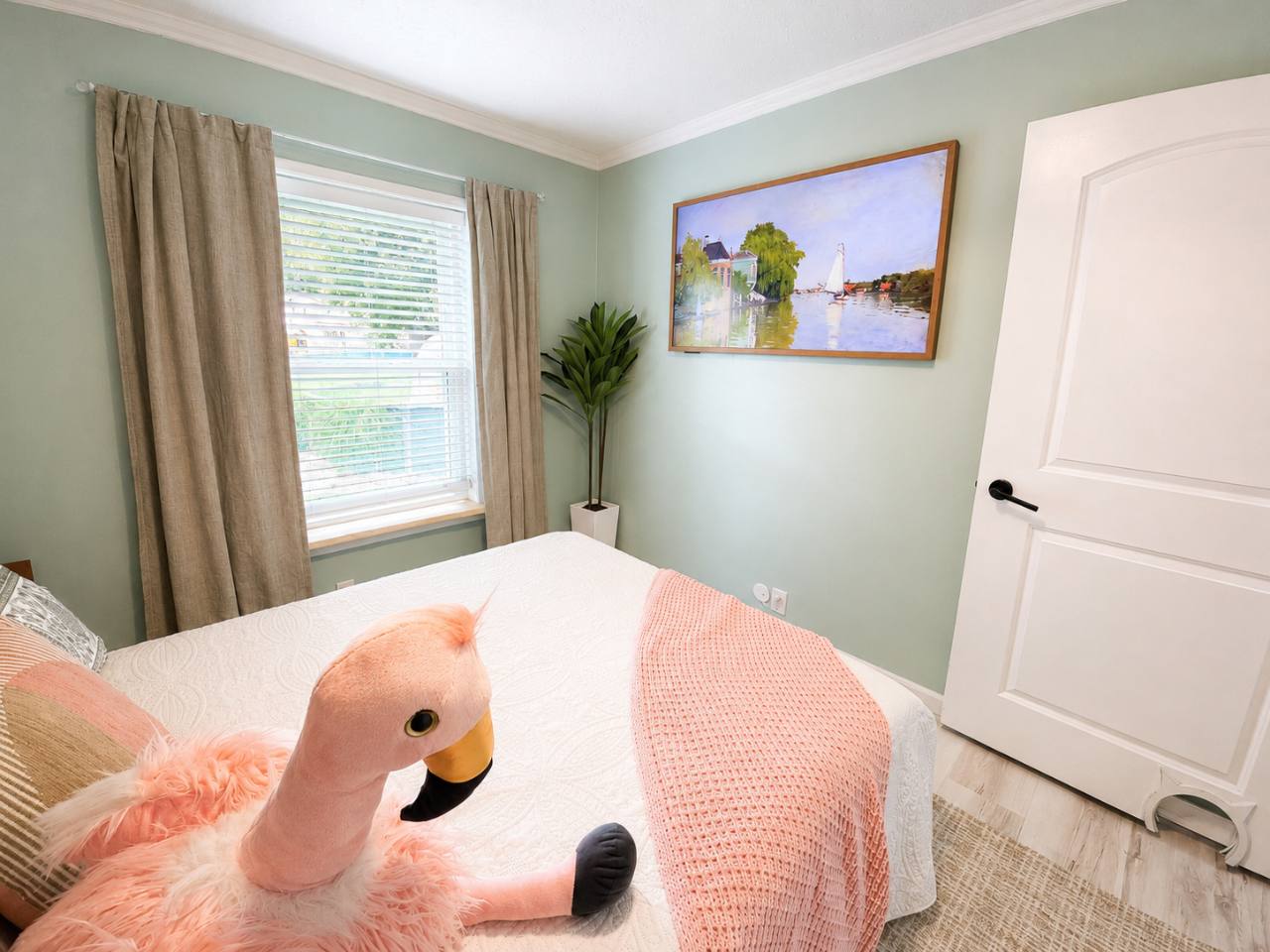 Boho bedroom with pink bedding, flamingo plush toy and a wall-mounted television displaying artwork