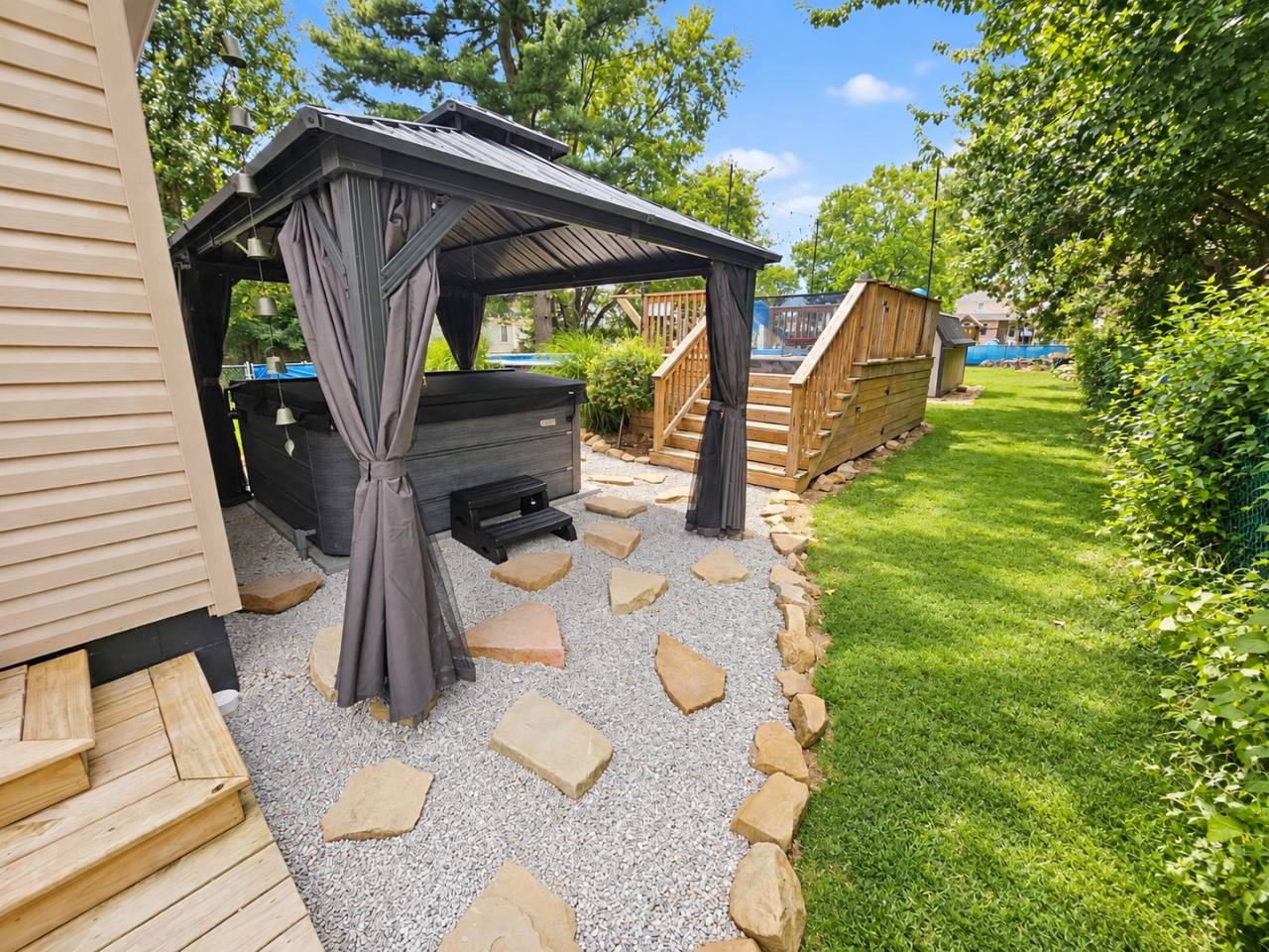 Curtained hot tub gazebo beside the house, with deck stairs and backyard lawn