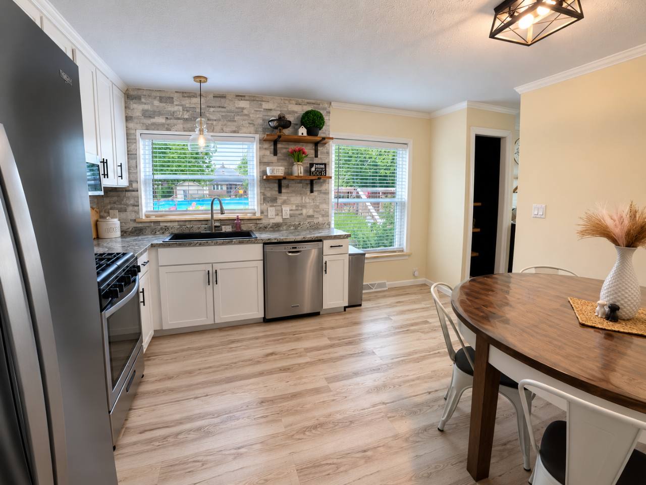 Kitchen sink and dishwasher beneath windows beside a wooden dining table