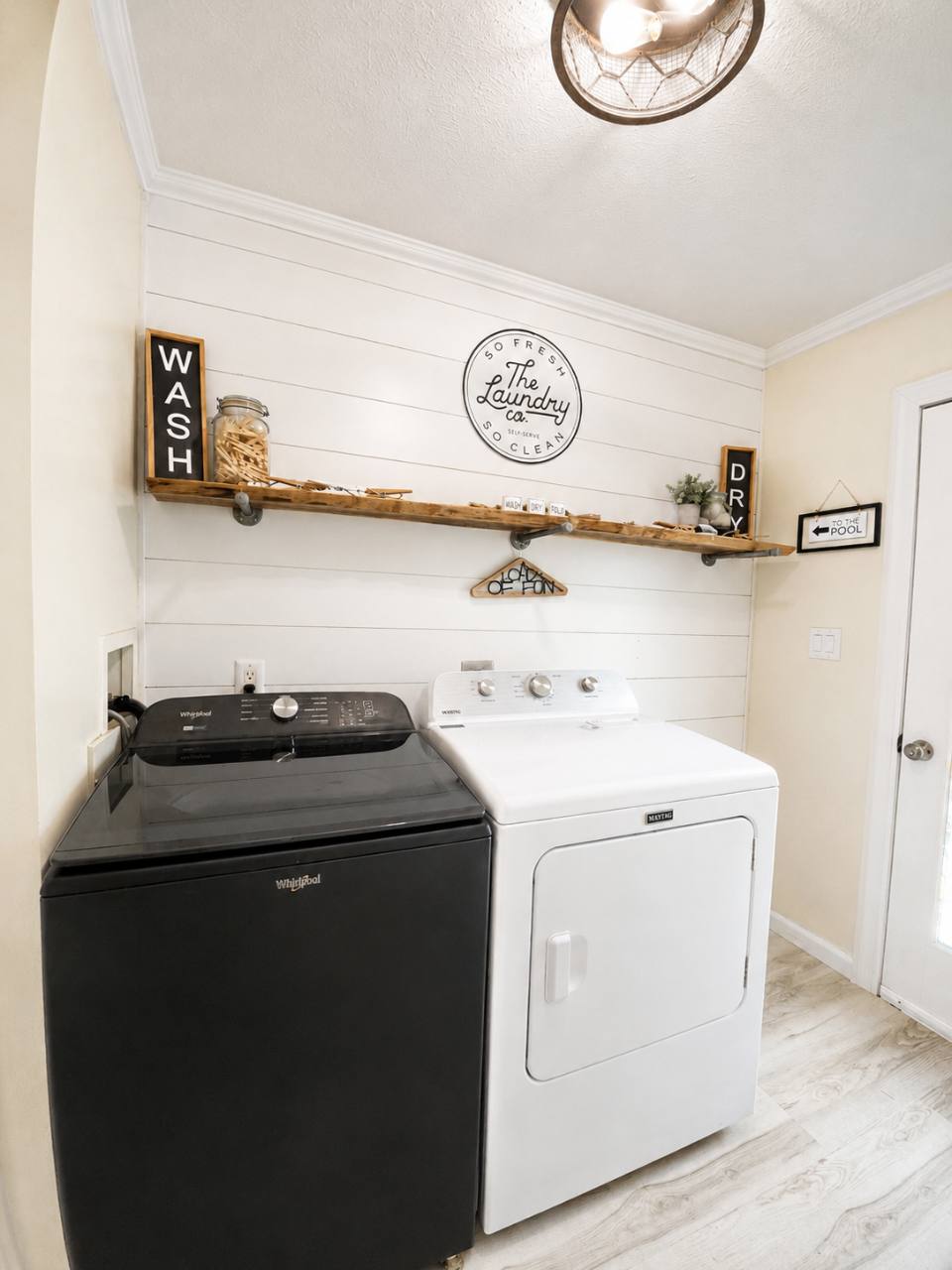 Laundry room with a black washing machine, white dryer and wooden shelf