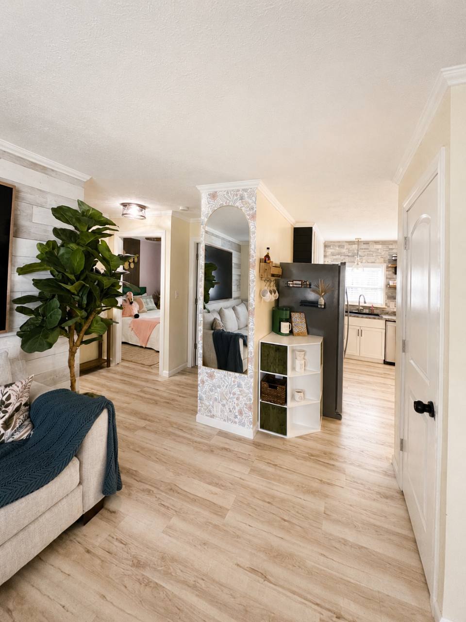 View from the living room toward the kitchen with refrigerator, coffee station and a bedroom doorway