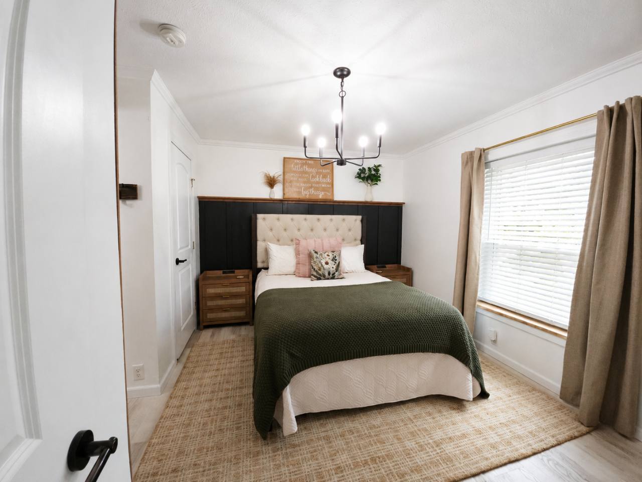 Bedroom with upholstered headboard, green blanket, wooden bedside tables and a black accent wall