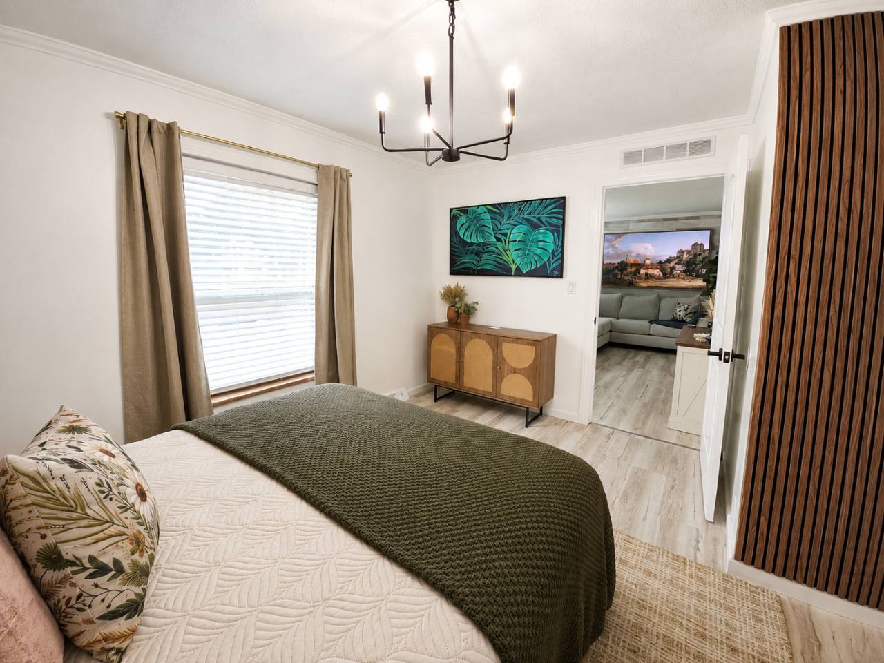 Bedroom with white bedding, green blanket, wooden dresser and a doorway toward the living room