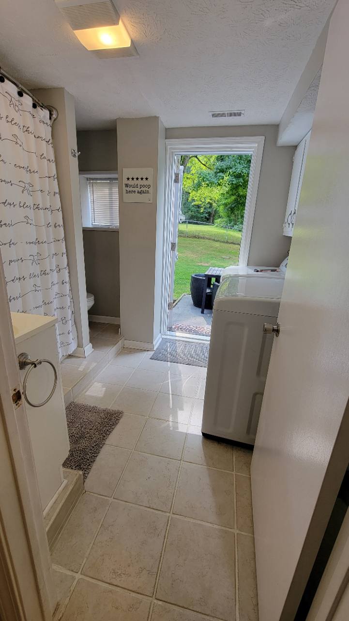 Bathroom and laundry area with shower curtain, washing machine and open door overlooking the backyard
