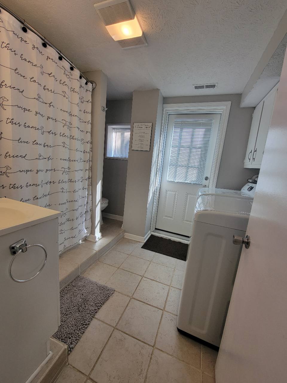 Bathroom and laundry area with vanity, shower curtain, washer and dryer beside a closed exterior door