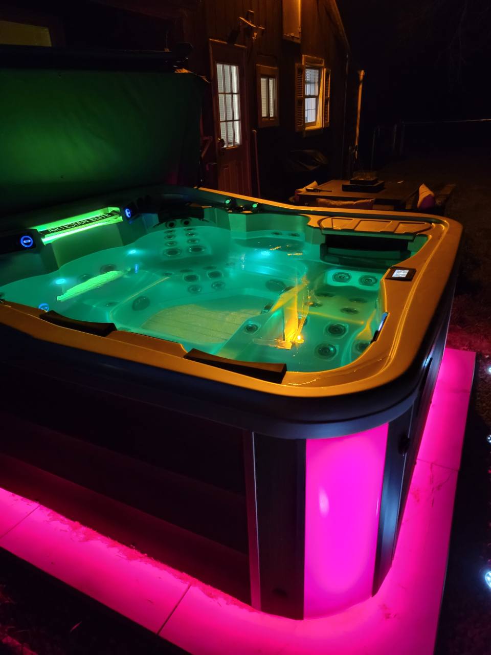 Hot tub at night with green lighting in the water and pink lighting around the base