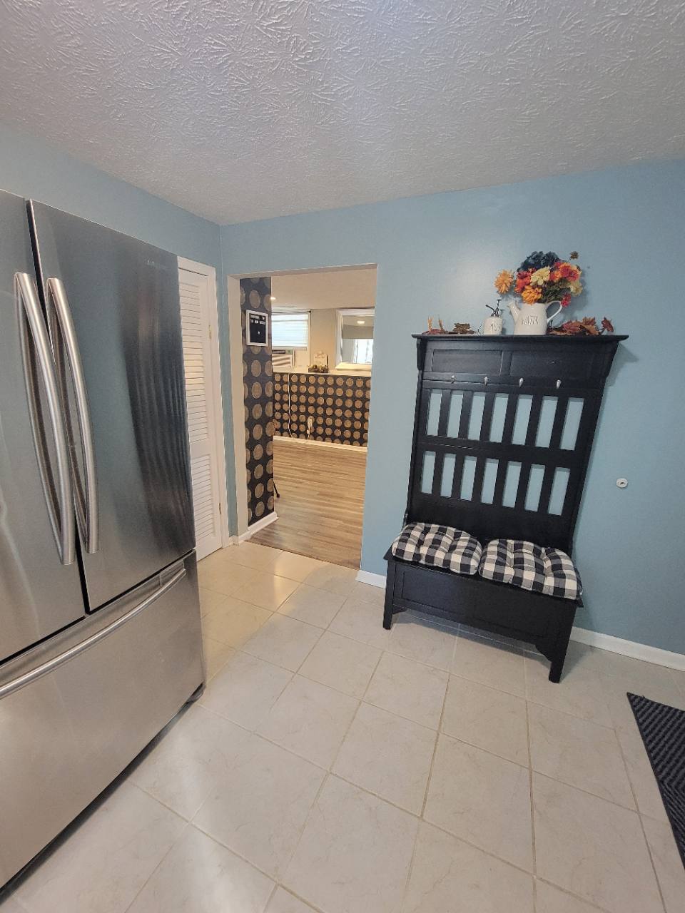 Kitchen with blue walls, stainless steel refrigerator and a black bench with checked cushions