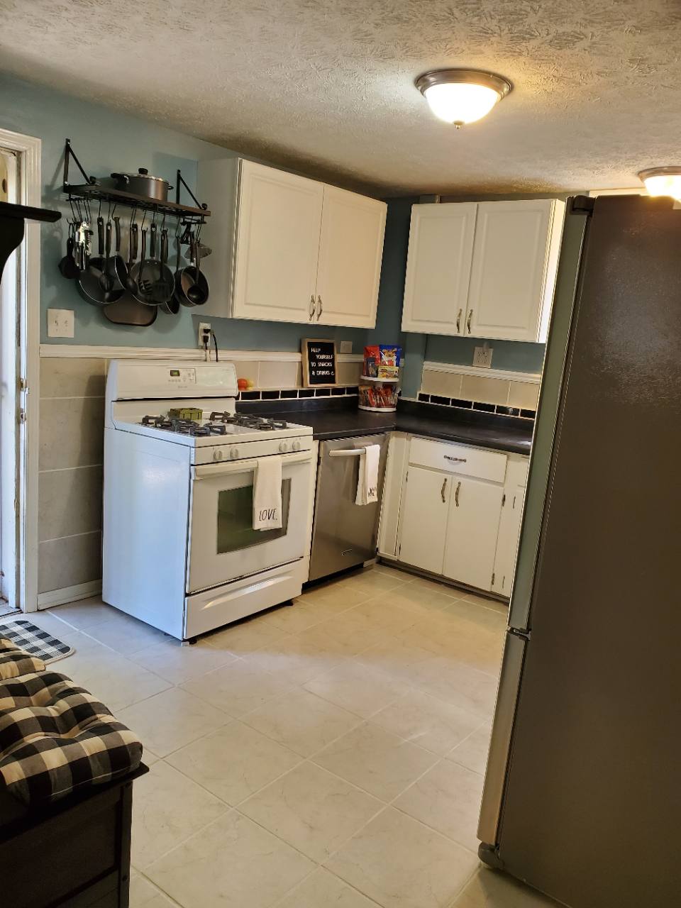 Kitchen with white gas range, dishwasher, hanging cookware and white cabinets