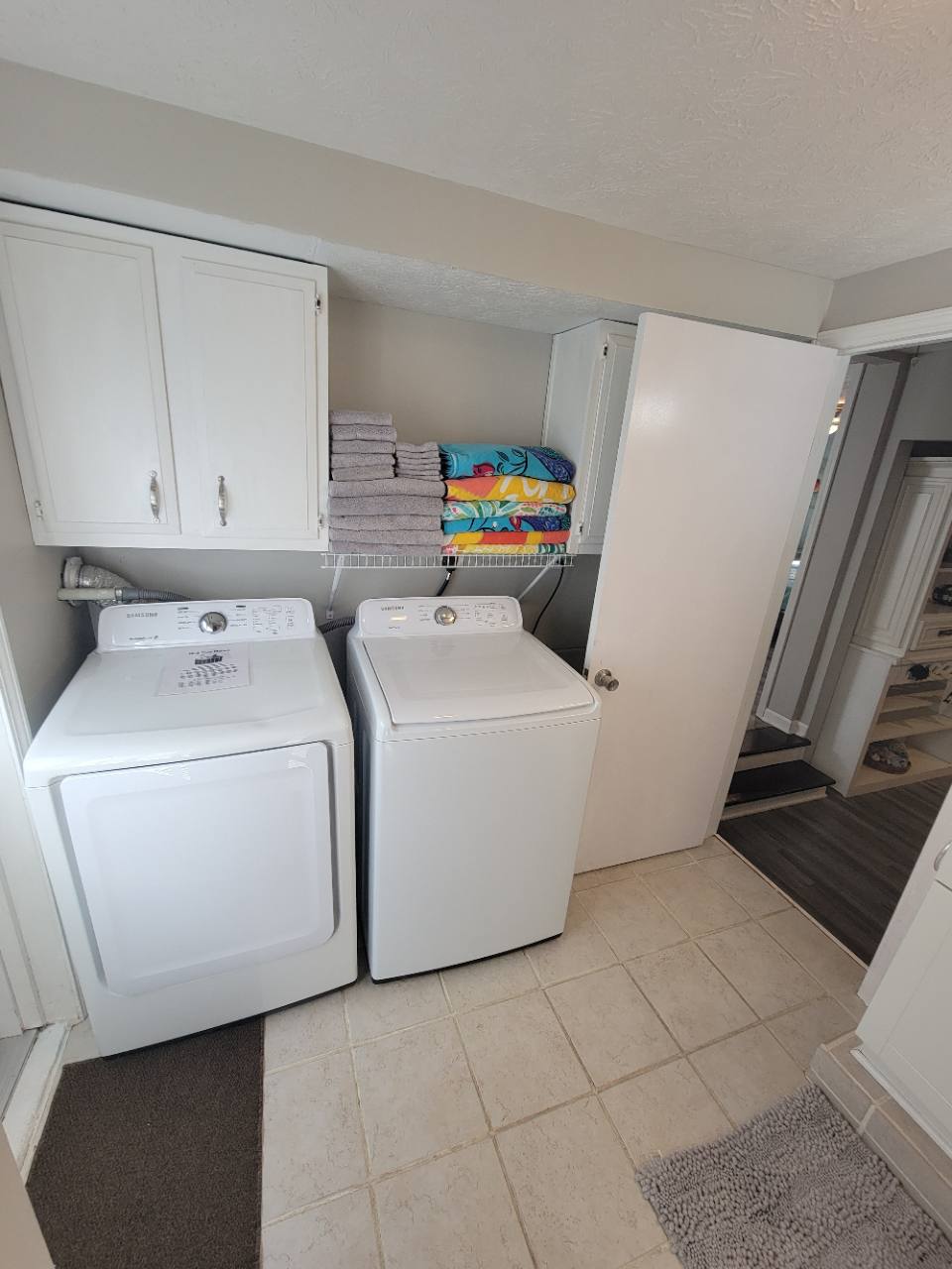 White washer and dryer below storage cabinets and shelves stacked with towels