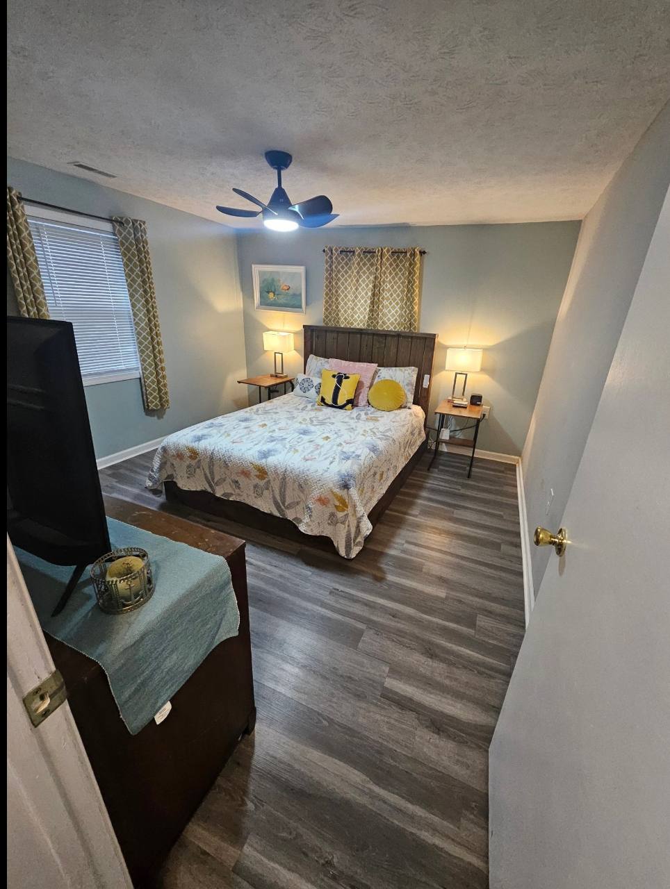 Primary bedroom viewed from the doorway with queen bed, wooden headboard, bedside lamps and ceiling fan