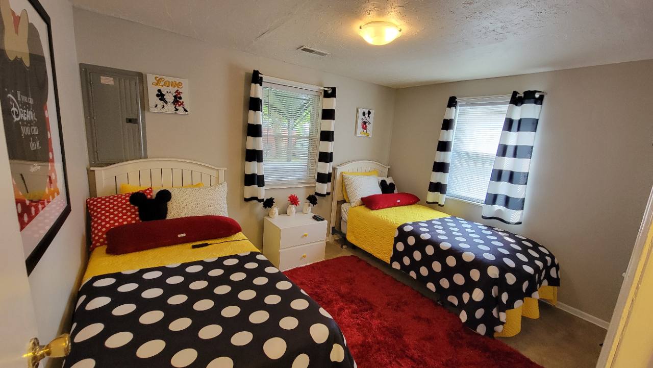 Two single beds with yellow bedding and black-and-white polka-dot blankets in the Mickey and Minnie-themed bedroom
