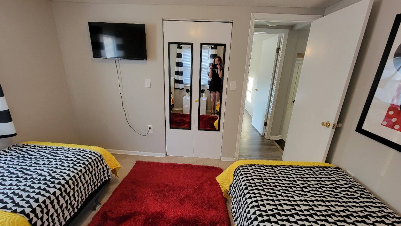 Twin bedroom with yellow bedding, black-and-white blankets, wall-mounted TV and mirrored closet doors